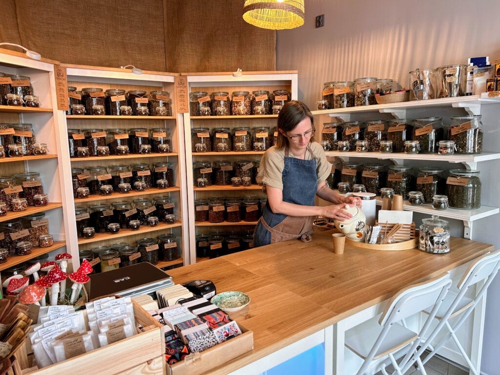 Zdjęcie przedstawiające wnętrze sklepu Esencja w Sanoku oraz ekspedientkę nalewającą herbatę do kubeczka degustacyjnego.