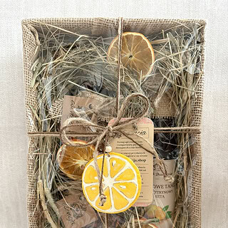 Zestaw prezentowy Cytrusowe Orzeźwienie zapakowany w naturalne materiały – jutę, celofan i suszone trawy. Wewnątrz znajduje się syrop cytrynowo-miętowy, susze owocowe oraz ręcznie malowana zawieszka w kształcie cytryny. Całość ozdobiona suszonymi plastrami cytrusów.