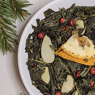 Zielona herbata Sencha Świąteczna Harmonia z pomarańczą, migdałami i różowym pieprzem na białym talerzyku, w świątecznej aranżacji.