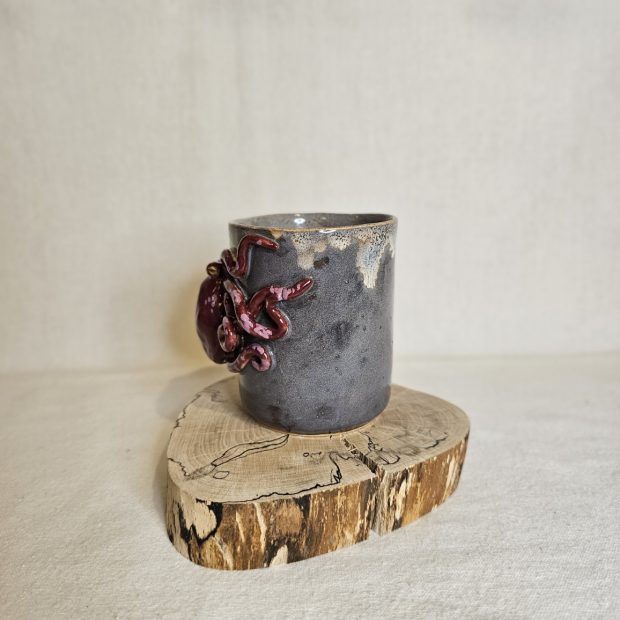 Kubek z karmazynową ośmiornicą na pieńku.