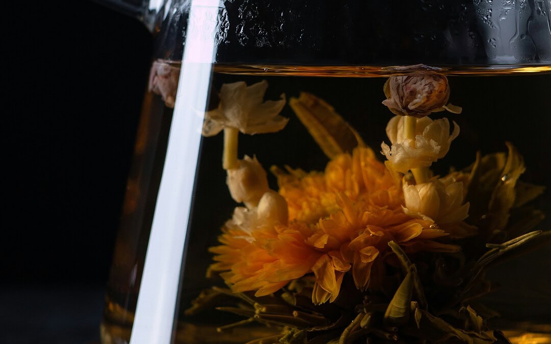 Zbliżenie na dzbanek szklany, w którym zaparzona jest kwitnąca herbata Kwiat Jaśminu i Lotosu.